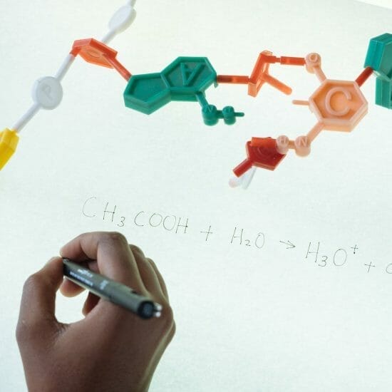 crop ethnic clever student writing formula after analysis of molecule model in university