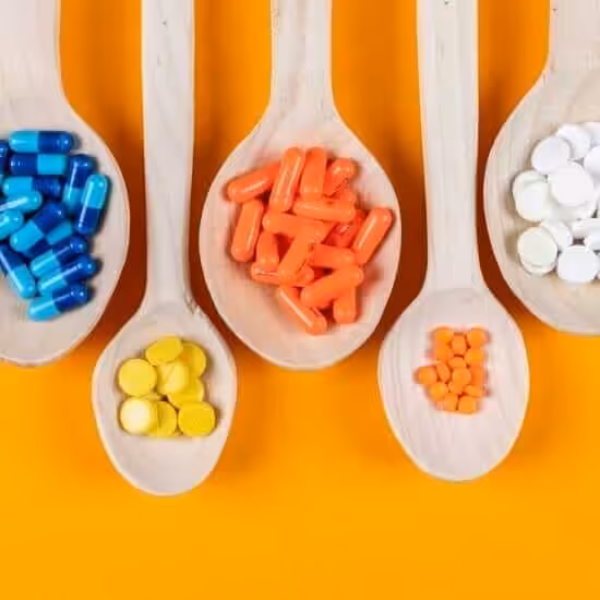 Top view colorful pills in wooden spoons on orange background. horizontal