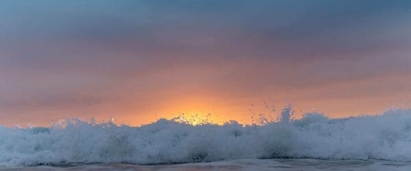 sunset sky over waving sea washing shore