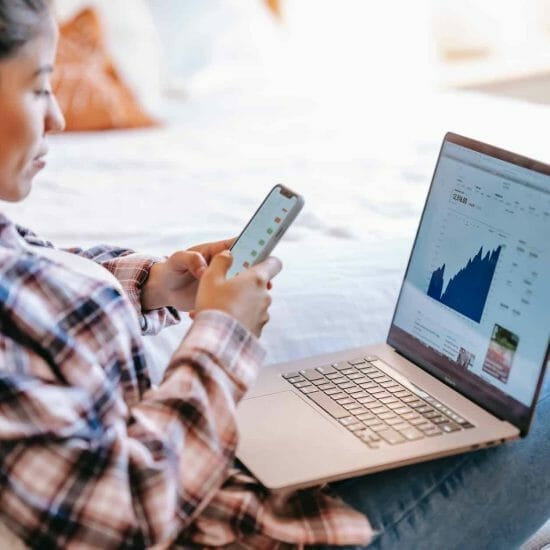 crop ethnic trader with smartphone and laptop on bench indoors