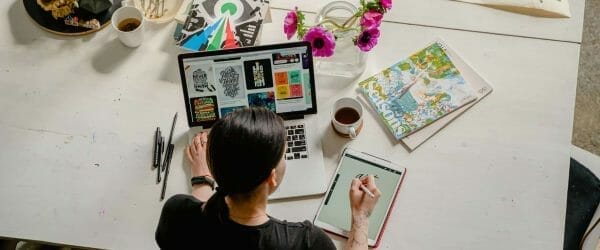 photo of woman writing on tablet computer while using laptop