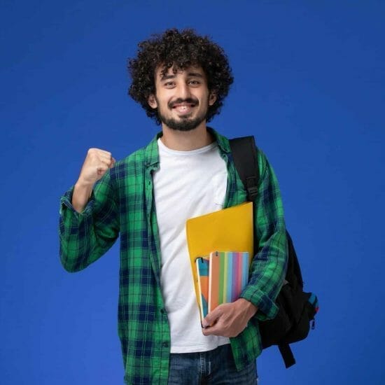 front view male student wearing black backpack holding copybooks files blue wall