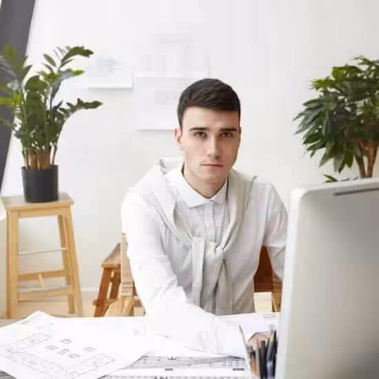 job career success concept indoor shot talented young male architect wearing white shirt sweater tied around his neck using cad program computer while working construction project