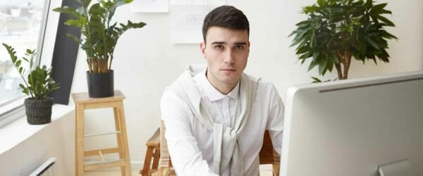 job career success concept indoor shot talented young male architect wearing white shirt sweater tied around his neck using cad program computer while working construction project