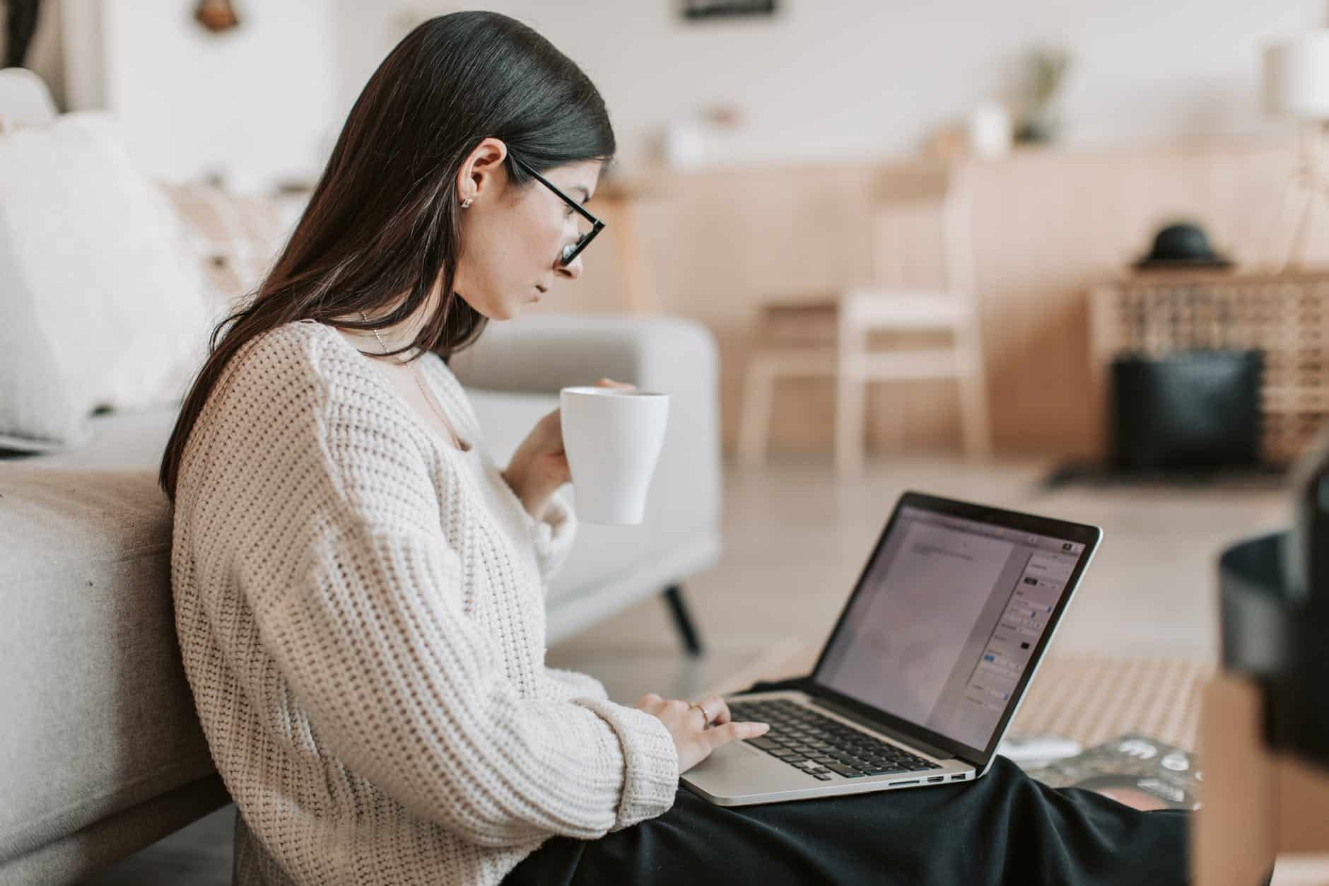 content young businesswoman using laptop while taking tea cup at home