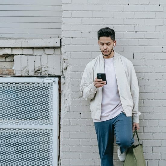 trendy indian man in earbuds chatting on smartphone in town