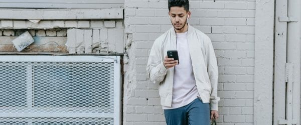 trendy indian man in earbuds chatting on smartphone in town