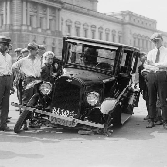 grayscale photo of people standing near the wrecked vintage car