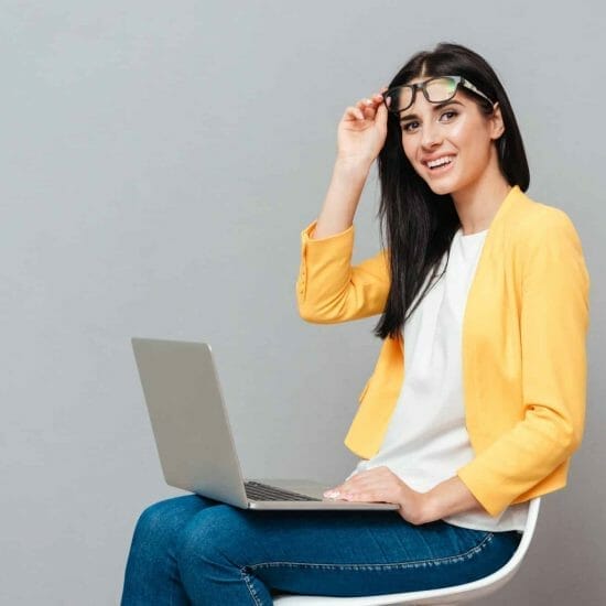 photo young pretty woman wearing eyeglasses dressed yellow jacket sitting stool while using laptop grey surface