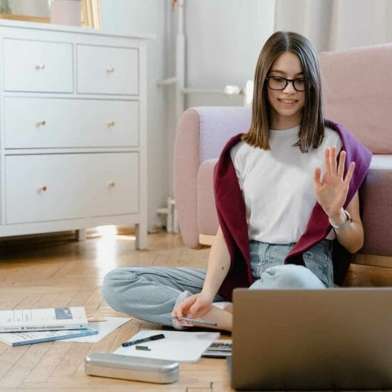 a woman in white shirt sitting on the floor while talking in front of her laptop