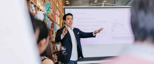 man in suit jacket standing beside projector screen