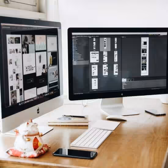 two imac s with keyboard and phones on desk