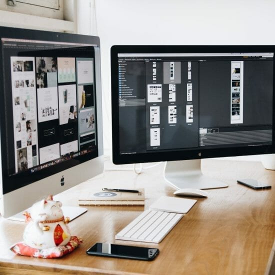 two imac s with keyboard and phones on desk