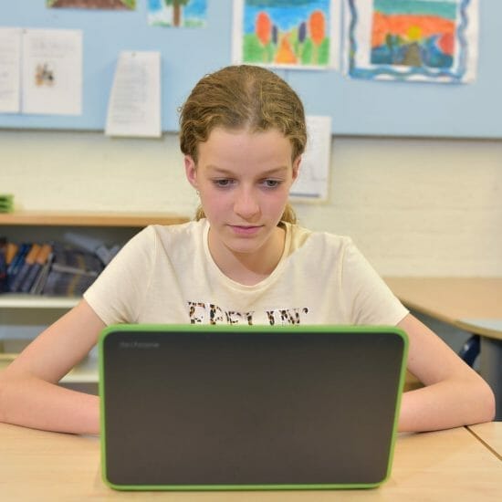 girl in white crew neck t shirt sitting at table using a laptop