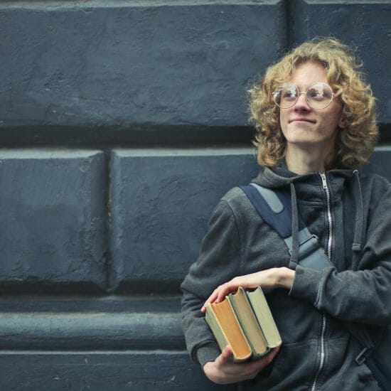 young man leaning against the wall holding a books