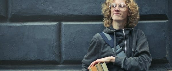 young man leaning against the wall holding a books