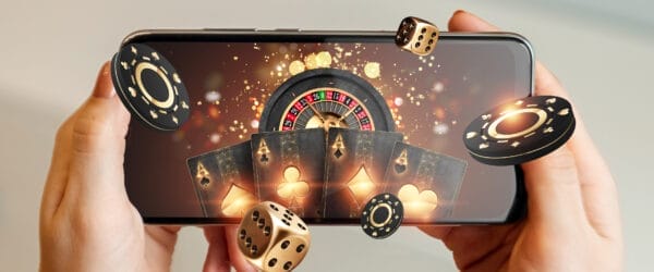 Creative background, online casino, in a man's hand a smartphone with playing cards, roulette and chips, black-gold background. Internet gambling concept. Copy space