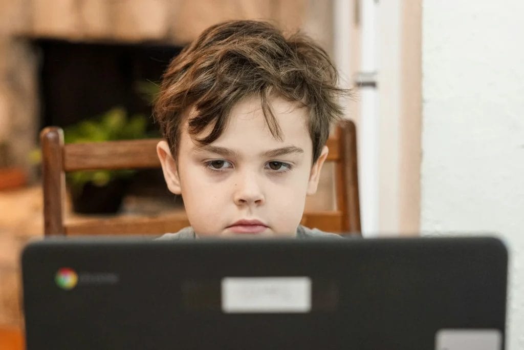 Showcasing Digital Education Trends - Kindergarten little boy student looking at a laptop computer while participating in distance home learning