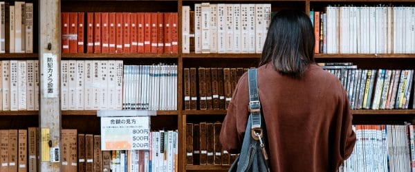 Woman Wearing Brown Shirt Carrying Black Leather Bag on Front of Library Books